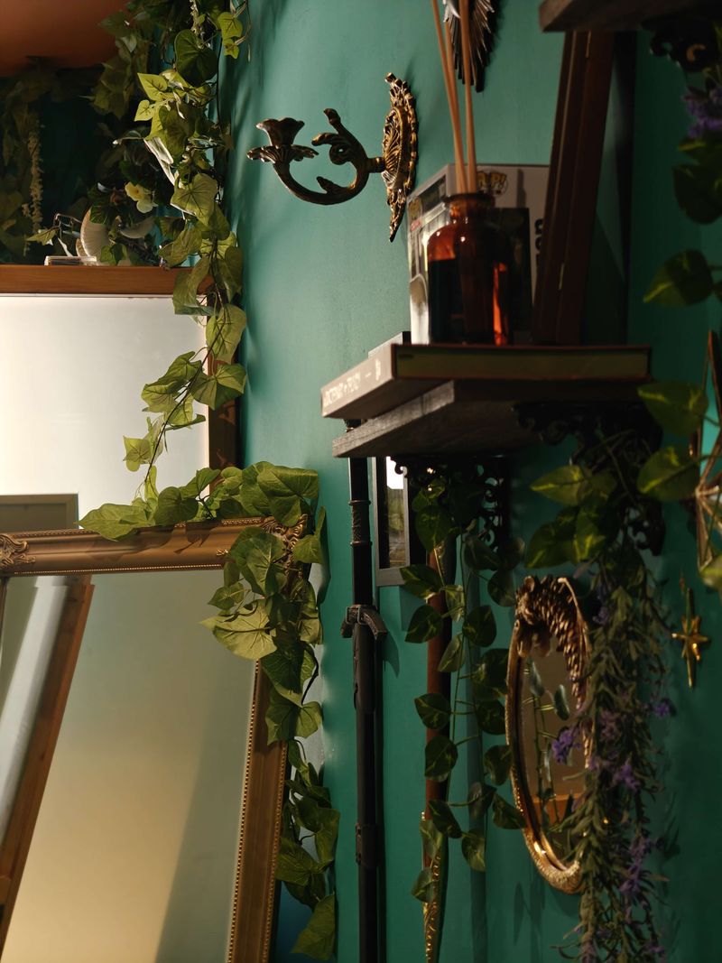 Warm light across gilded mirrors wrapped in ivy, a brass candle sconce and an amber apothecary bottle on a wooden shelf